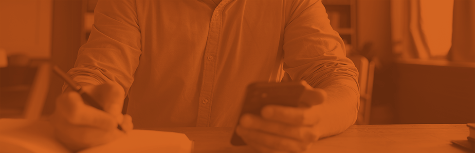 orange-scale image of person holding a phone in one hand and a pen in the other hand