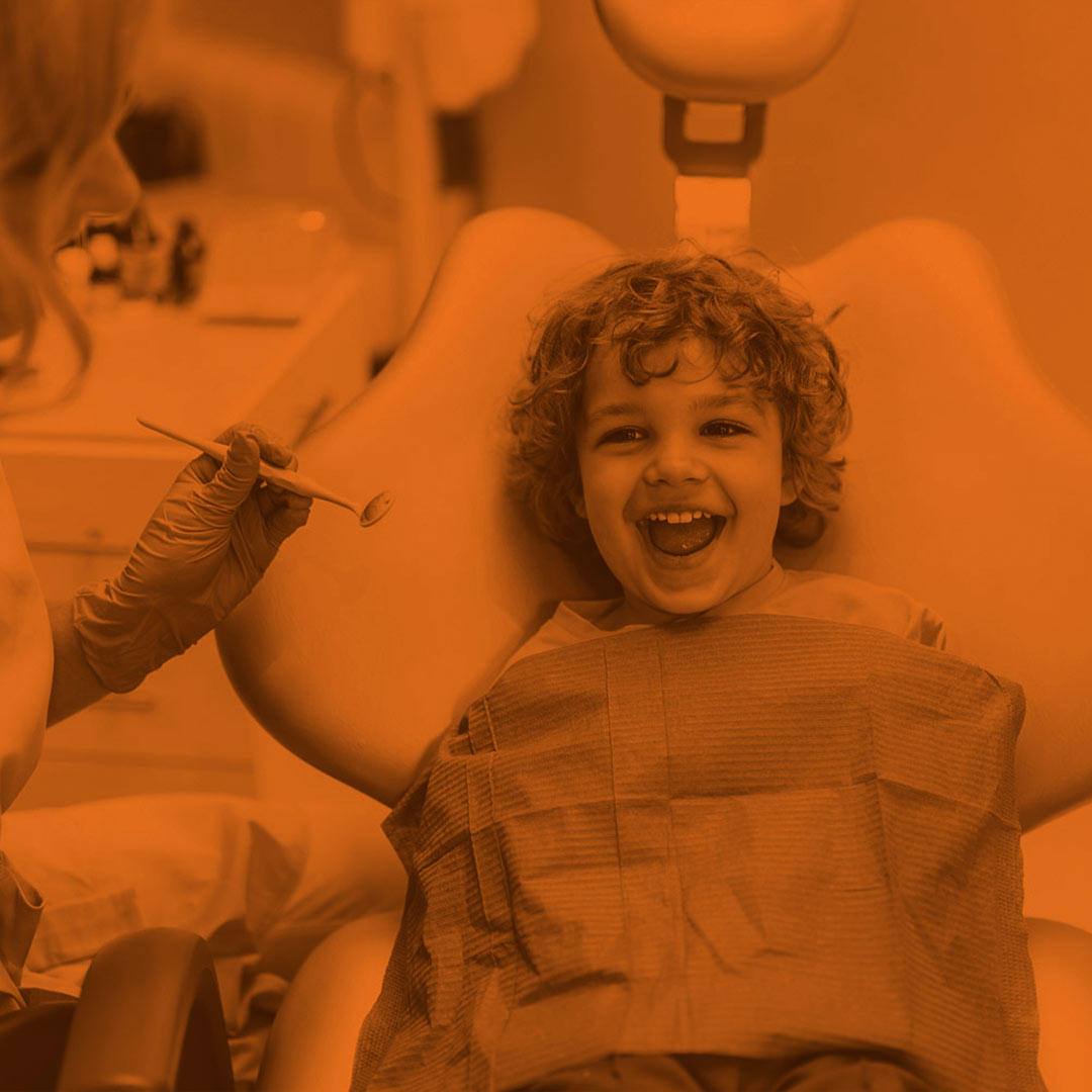 orange-scale image of a child in a dental chair with a dentist on the left side