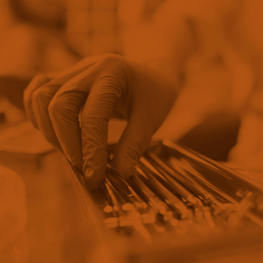 orange-scale image of hands reaching into a tray of dental tools