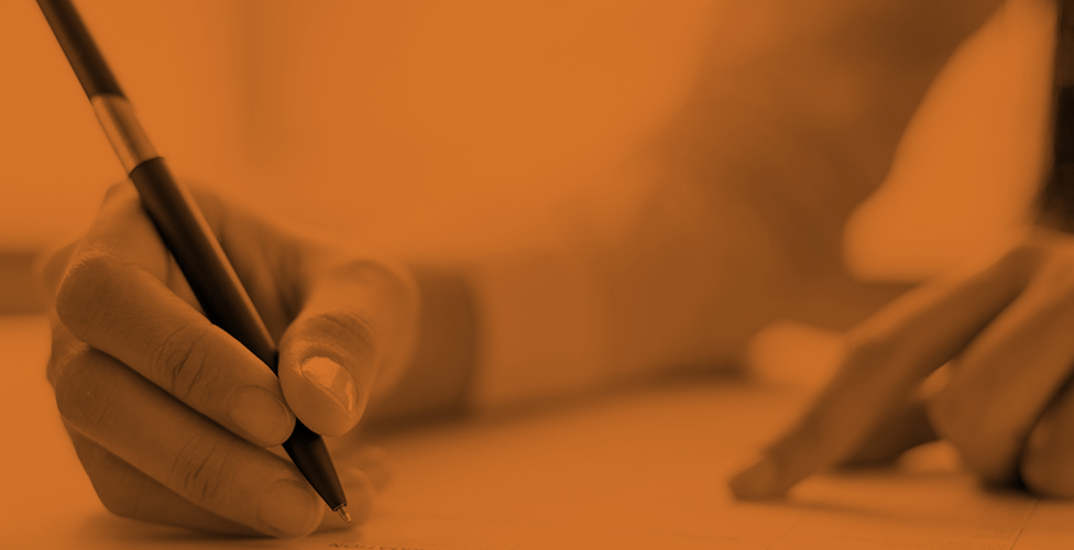 orange-scale image of a hand holding a pen poised to write