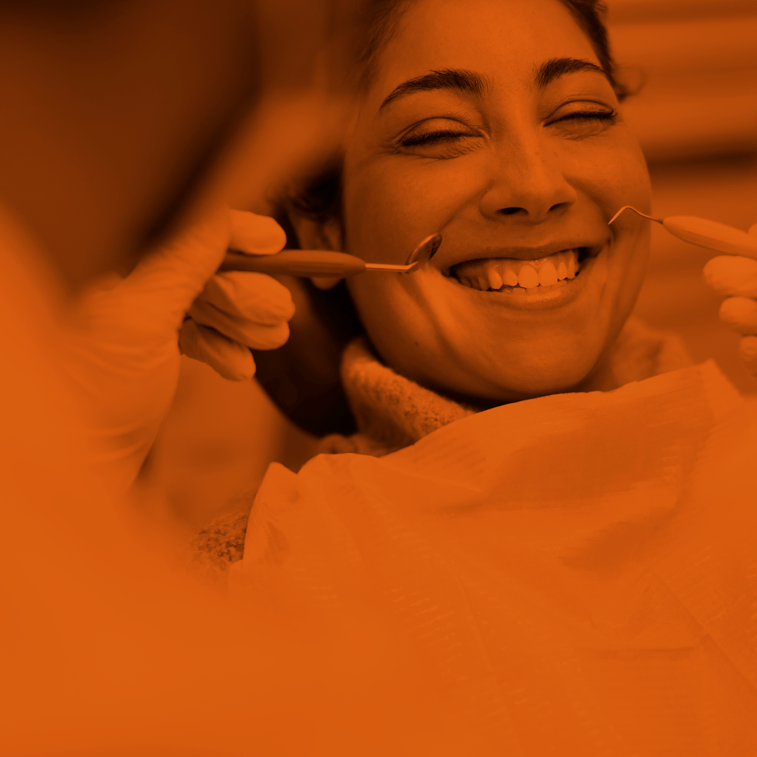 orange-scale image of a woman smiling with the back of a dentist in the foreground